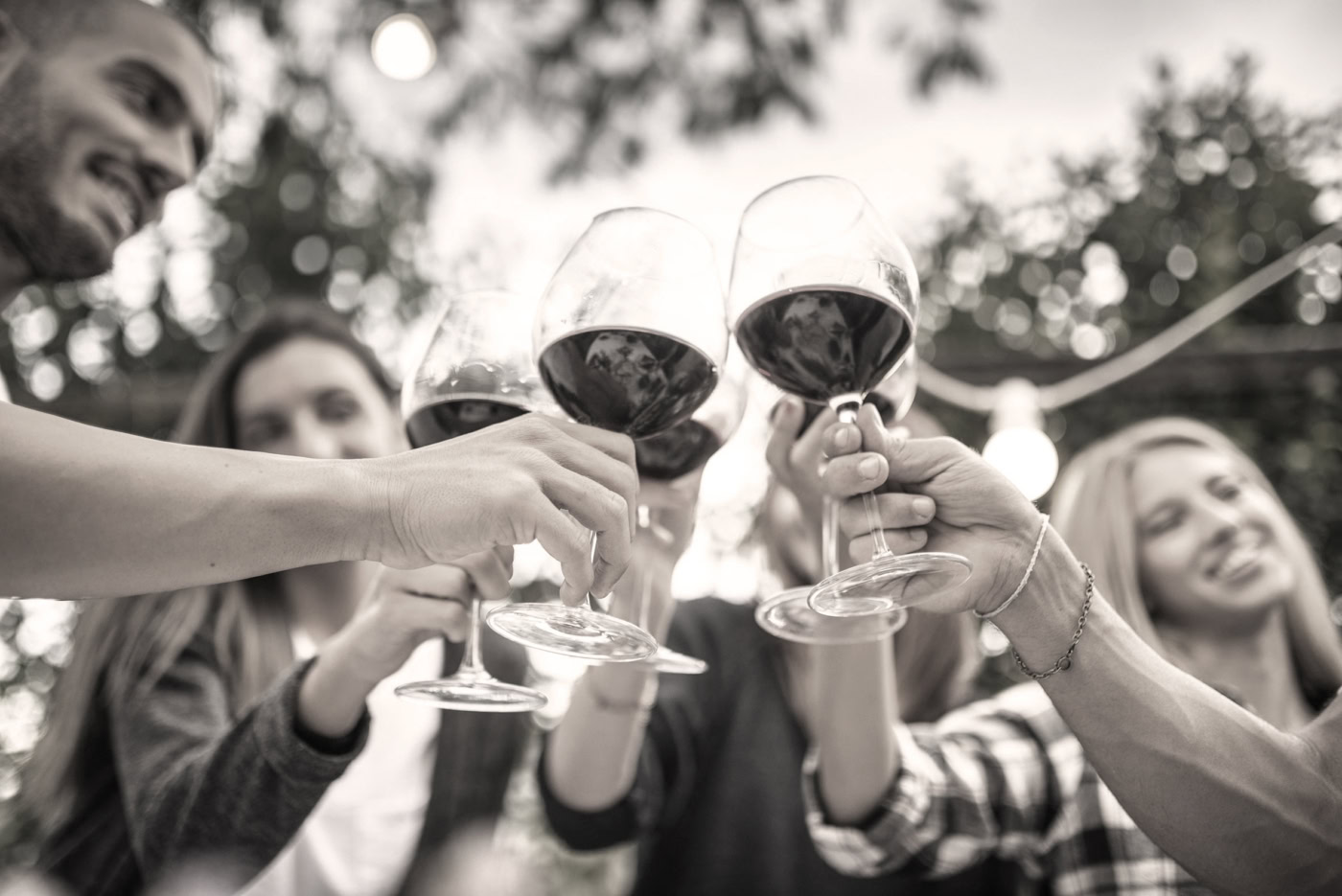 Group of friends clinking glasses of red wine outdoors at night.