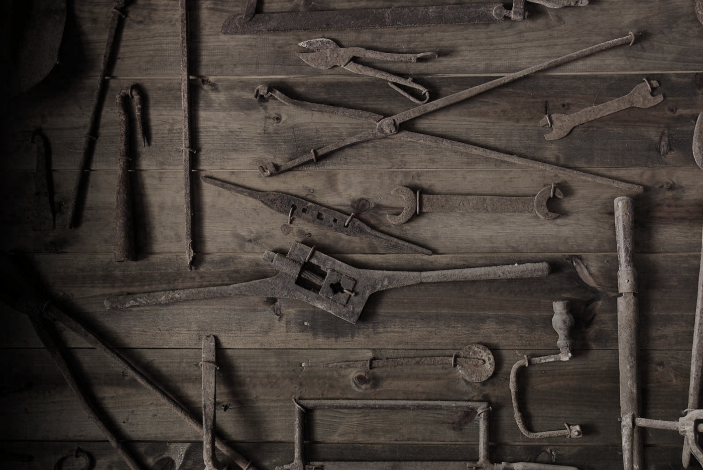 Assorted vintage hand tools including wrenches, hammers, and screwdrivers laid out on a wooden surface.